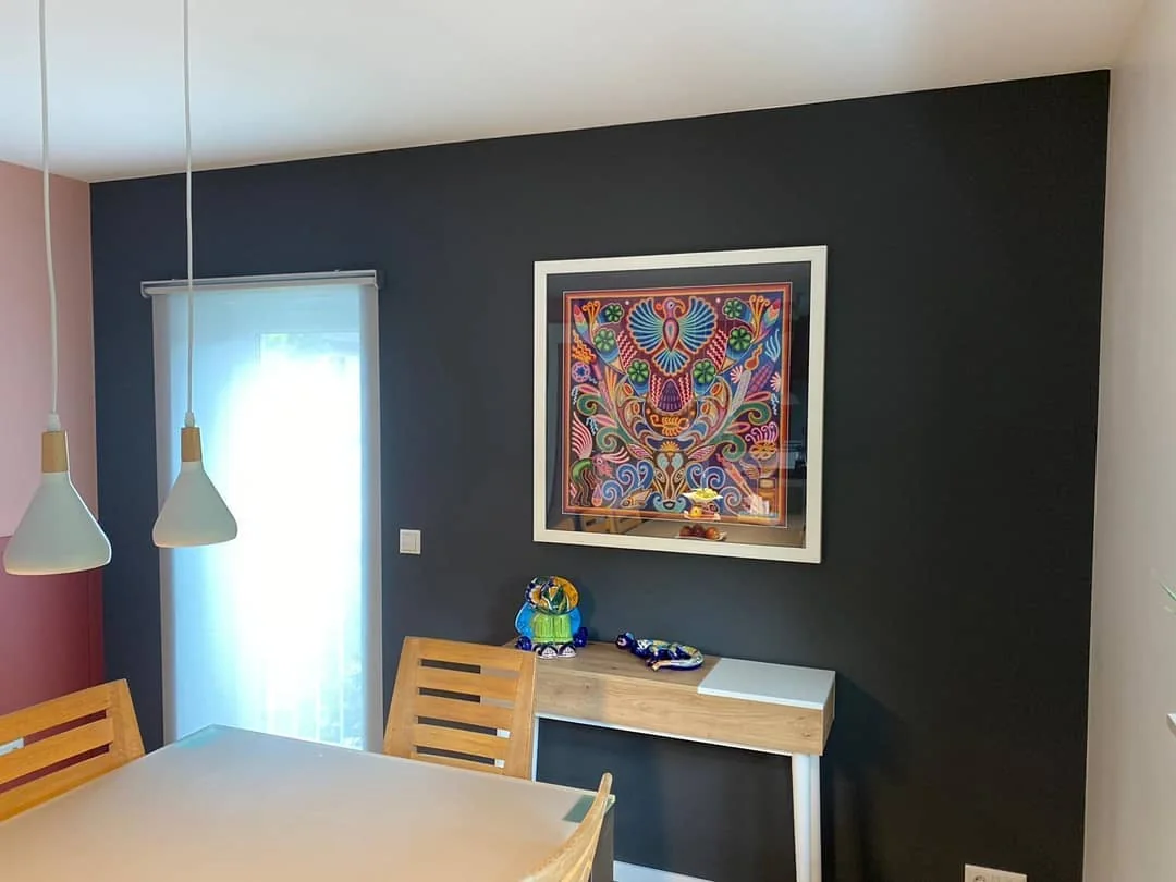 Esszimmer mit dunkler Wand, farbenfroher gerahmter Kunst und Pendelleuchten