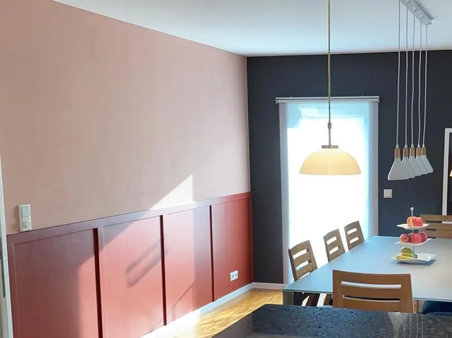 Esszimmer mit rosafarbenen Wandflächen, hellem Tisch und Leuchten