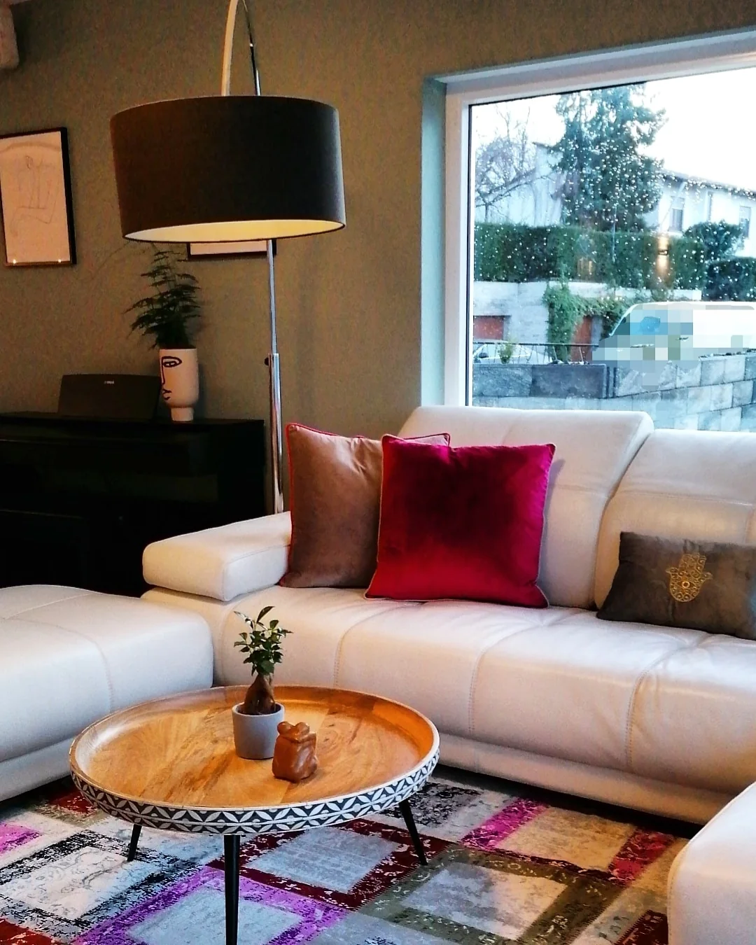 Wohnzimmer mit hellem Sofa, kräftigen Akzentkissen und rundem Holztisch